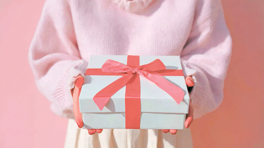 A close-up of a person holding out a neatly wrapped white gift box with a deep red ribbon