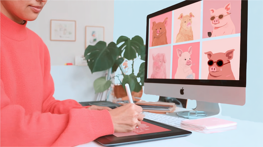 Digital female artist in a coral sweater drawing cartoon pig illustrations on a tablet, with six pig portraits displayed on a desktop screen in a modern, creative workspace.