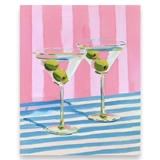 Two martini glasses with olives on a pink and blue striped background