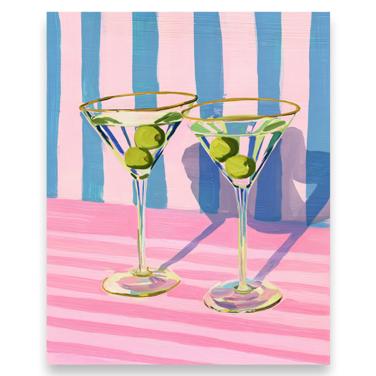 Two martini glasses with olives on a pink and blue striped background